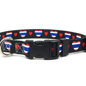 May include: Black dog collar with a repeating pattern of red hearts and hearts with the colors of the Thai flag. The collar has a black plastic buckle and a silver metal D-ring for leash attachment.
