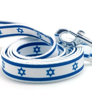 May include: A white and blue dog leash with a silver clip. The leash is decorated with a repeating pattern of blue stars of David.