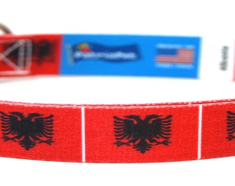 May include: Red dog collar with a repeating pattern of the Albanian flag. The collar has a black buckle and a silver ring.