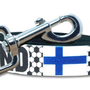 May include: A black and white dog leash with a soccer ball pattern and a Finnish flag design. The leash has a silver metal clip.