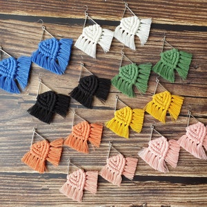 May include: A collection of 12 pairs of triangle-shaped earrings with fringe. The earrings are made of macrame and come in a variety of colors, including blue, green, yellow, orange, pink, and black.