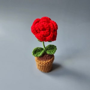May include: A crocheted red rose in a brown pot with green leaves.