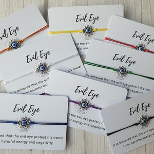 May include: Assortment of colorful string bracelets with silver evil eye charms. Each bracelet is accompanied by a card with the text "Evil Eye" and a description of the evil eye's protective properties.