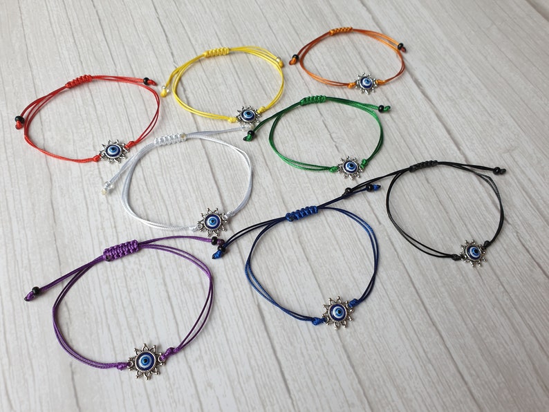 May include: Eight colorful string bracelets with a silver evil eye charm. The bracelets are red, yellow, orange, green, white, blue, purple, and black.