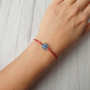 May include: Red string bracelet with a silver charm featuring a blue evil eye symbol.