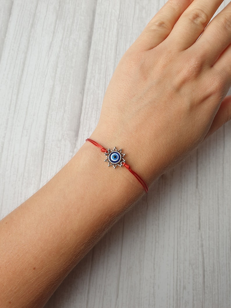 May include: Red string bracelet with a silver charm featuring a blue evil eye symbol.