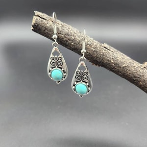 May include: A pair of silver dangle earrings with turquoise stones. The earrings have a teardrop shape with intricate silver designs.