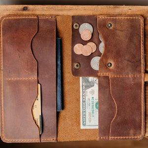 May include: A brown leather wallet with multiple pockets and a strap. The wallet is open and contains a passport, credit card, cash, and coins.