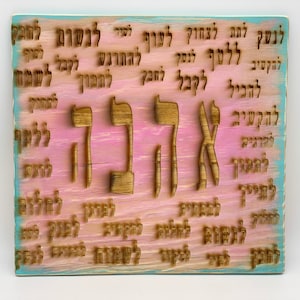 May include: A wooden sign with a light blue and pink background. The sign has the Hebrew word "Ahava" carved into it, which means "love" in English. The word is surrounded by other Hebrew words.