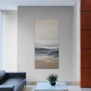 May include: Abstract painting of a seascape with shades of blue, gray, and beige. The painting is hanging on a wall in a modern living room setting.