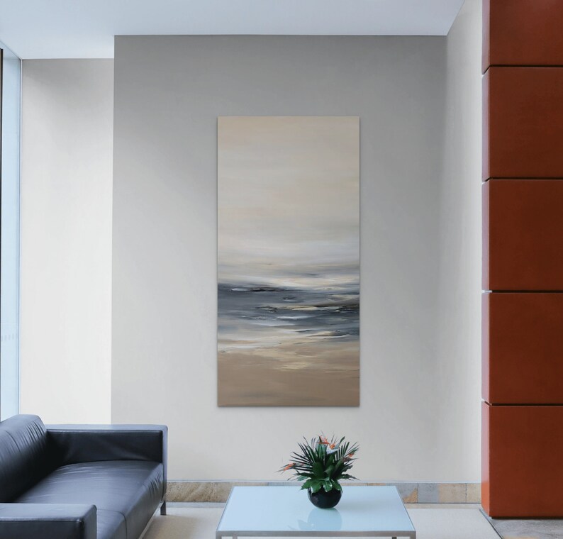 May include: Abstract painting of a seascape with shades of blue, gray, and beige. The painting is hanging on a wall in a modern living room setting.