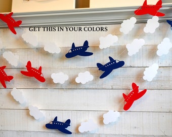 May include: A red, white, and blue airplane garland with clouds. The garland features red and blue airplanes with white clouds.