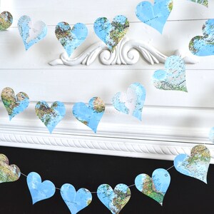 May include: A garland of blue paper hearts with a world map design. The hearts are strung together with white string and are hanging from a white wall.