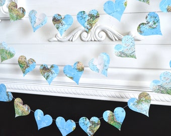 May include: A garland of blue paper hearts with a world map design. The hearts are strung together with white string and are hanging from a white wall.