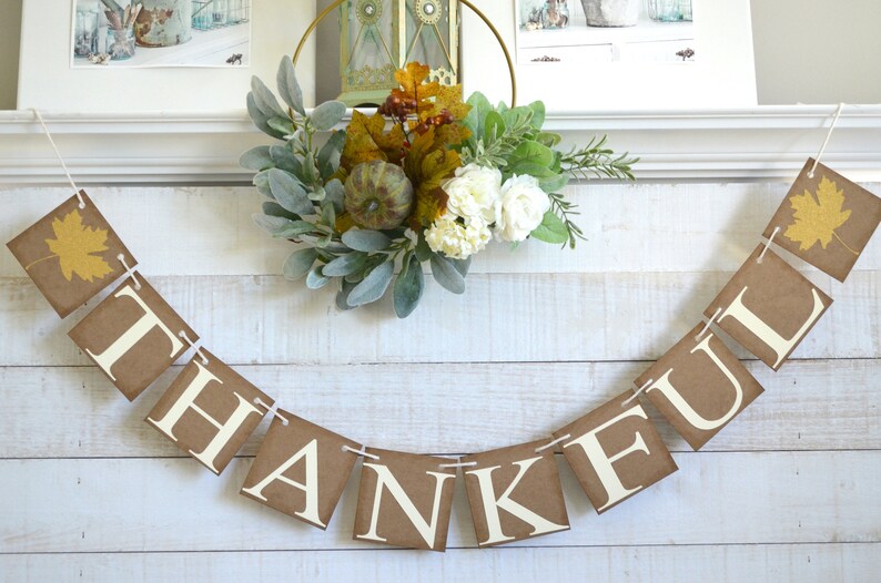 K&ouml;nnte beinhalten: Ein braunes Papierbanner mit dem Wort "THANKFUL" in wei&szlig;en Buchstaben. Das Banner ist mit Schnur befestigt und mit Herbstbl&auml;ttern verziert.