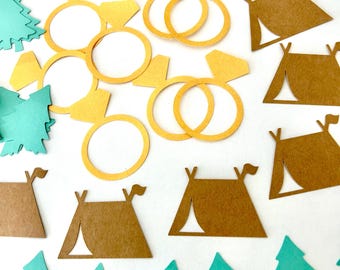 May include: Assortment of paper cutouts in the shape of pine trees, tents, and rings. The trees are teal green, the tents are brown, and the rings are yellow.