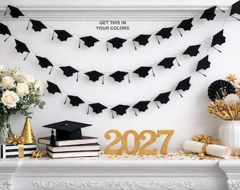 May include: A black graduation cap banner with three draped strings of caps, a stack of books topped with a single graduation cap, and gold glitter numbers reading 2027. The text GET THIS IN YOUR COLORS is printed in black above the banner.