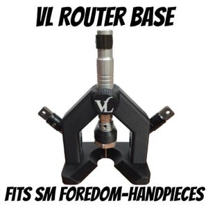 May include: A black VL router base with a silver central column and two side attachments. The text VL ROUTER BASE and FITS SM FOREDOM-HANDPIECES is printed in black. The device features a central adjustment knob with a VL logo and a U-shaped base.