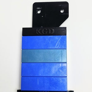 May include: A stack of blue and gray plastic blocks with a black plastic top piece. The top piece has the letters "KGD" printed on it.