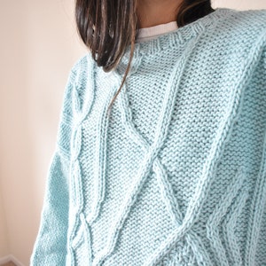 Könnte beinhalten: Ein hellblauer Pullover mit Zopfmuster und Rundhalsausschnitt.