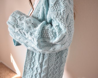 May include: A light blue knitted cardigan with a cable knit pattern. The cardigan is open in the front and has long sleeves.