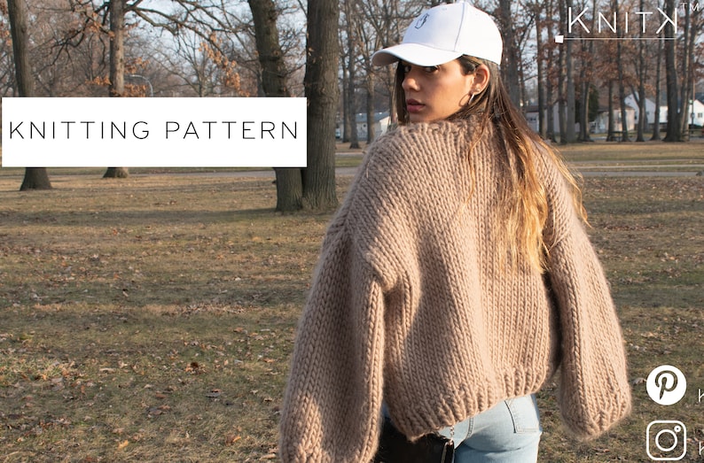 May include: A beige, chunky knit jumper with a wide neckline and long sleeves. The words "KNITTING PATTERN" are in a white rectangle. The jumper is worn by a person wearing a white baseball cap.