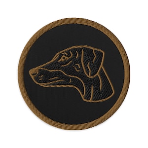 May include: Embroidered patch featuring a dog's profile in brown thread on a black circular background. The patch has a brown border. The dog's head is facing left, with detailed stitching outlining its features. This patch is suitable for jackets, bags, or other fabric items.