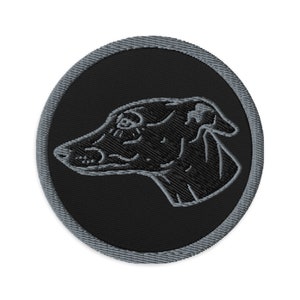 Op de afbeelding: Geborduurde patch met een windhondprofiel in zwart garen op een zwarte cirkelvormige achtergrond. De patch heeft een grijze rand. Het ontwerp is gedetailleerd en geschikt voor toepassing op kleding of accessoires.