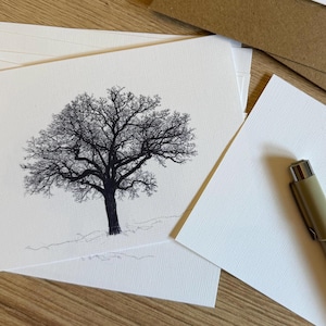 May include: A stack of white cards with a black and white tree illustration. A pen rests on the cards. The tree is detailed with many branches and a thick trunk. The cards are on a wooden surface.