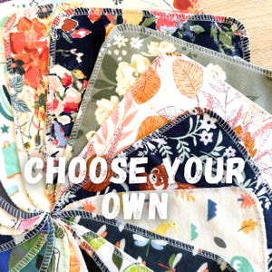 May include: A collection of square fabric cloths arranged in a fan shape, featuring various floral, botanical, and animal patterns in colors including navy, orange, green, and white. The edges are finished with dark stitching. Text reads CHOOSE YOUR OWN.