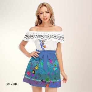 Puede incluir: Una blusa blanca con hombros descubiertos con ribete de encaje negro y un diseño floral, combinada con una falda azul con un colorido estampado floral y de mariposas. La falda tiene una cinta azul en la cintura. Tallas XS - 2XL.