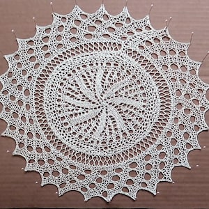 May include: A white crocheted doily with a circular design and a scalloped edge.