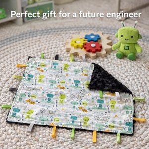 May include: A baby blanket with a robot pattern, black plush backing, and colorful ribbons. A green robot plush toy and a wooden gear toy are also in the image. The text "Perfect gift for a future engineer" is visible.