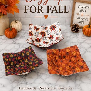 May include: Three fabric bowl cozies featuring seasonal patterns. One displays turkeys with the text GOBBLE TIL YOU WOBBLE, another has dark brown fabric with colorful autumn leaves, and the third features orange fabric with a dense pattern of fall leaves.