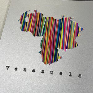 May include: A silver laptop with a colorful sticker of the Venezuela map. The sticker is filled with vertical lines of various colors. The word "Venezuela" is printed in a small, black font below the sticker.