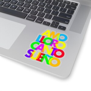 May include: A sticker with the Spanish words "AMO", "LLORO", "CANTO", and "SUE&Ntilde;O" stacked on top of each other. The words are in different colors, including red, yellow, green, blue, and pink.