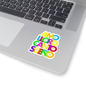 May include: A colorful sticker with the Spanish words "AMO", "LLORO", "CANTO", and "SUENO" stacked on top of each other. The words are in a rainbow of colors, with each word having a different color.