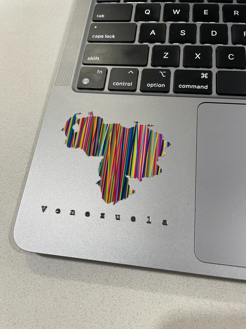 May include: A silver laptop with a colorful sticker of the Venezuela map. The sticker is filled with vertical lines of various colors. The word "Venezuela" is printed in a small, black font below the sticker.