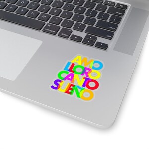 May include: A sticker with the Spanish words "AMO", "LLORO", "CANTO", and "SUE&Ntilde;O" stacked on top of each other. The words are in different colors, including red, yellow, blue, green, and purple.