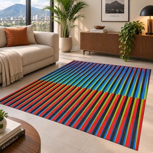 Puede incluir: Una alfombra rectangular que presenta un patrón vibrante de rayas verticales en colores alternos de rojo, negro, azul y verde. El diseño está dividido en dos secciones distintas con rayas que corren en diferentes direcciones sobre el suelo.