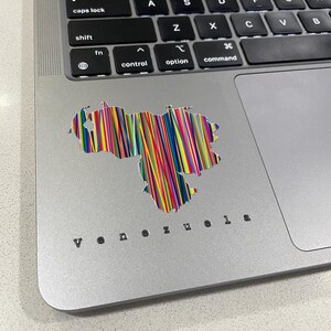 May include: A laptop with a colorful sticker of the Venezuela map. The sticker is made of vertical lines in various colors. The word "Venezuela" is printed in a small, black font below the sticker.