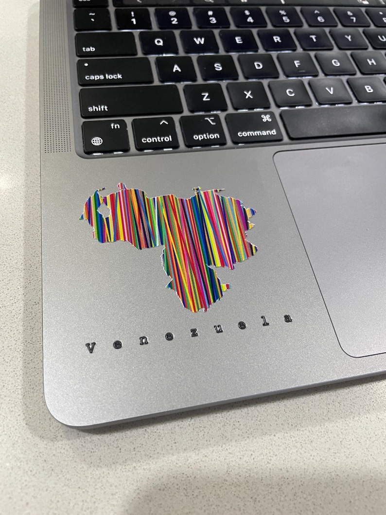May include: A laptop with a colorful sticker of the Venezuela map. The sticker is made of vertical lines in various colors. The word "Venezuela" is printed in a small, black font below the sticker.
