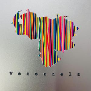 May include: A silver-colored artwork featuring the outline of Venezuela filled with vertical stripes in various colors. The word "Venezuela" is printed in black letters below the map.