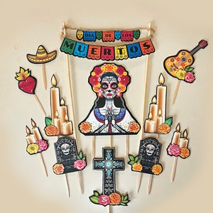 Könnte beinhalten: Tortenaufleger-Set zum Tag der Toten mit einem Zucker Schädel, Kerzen, einer Gitarre, einem Grabstein, einem Kreuz und einem Sombrero. Das Banner lautet "Dia de los Muertos".