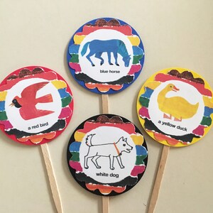 May include: Four colorful cupcake toppers with images of a blue horse, a red bird, a yellow duck, and a white dog. Each topper has a scalloped edge and a rainbow stripe design. The text on each topper reads "blue horse", "a red bird", "a yellow duck", and "white dog".
