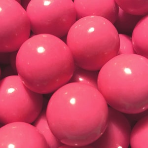 May include: A close-up shot of a pile of bright pink, smooth, spherical objects. The spheres have a glossy finish and reflect light. The objects are tightly packed together, filling the frame.