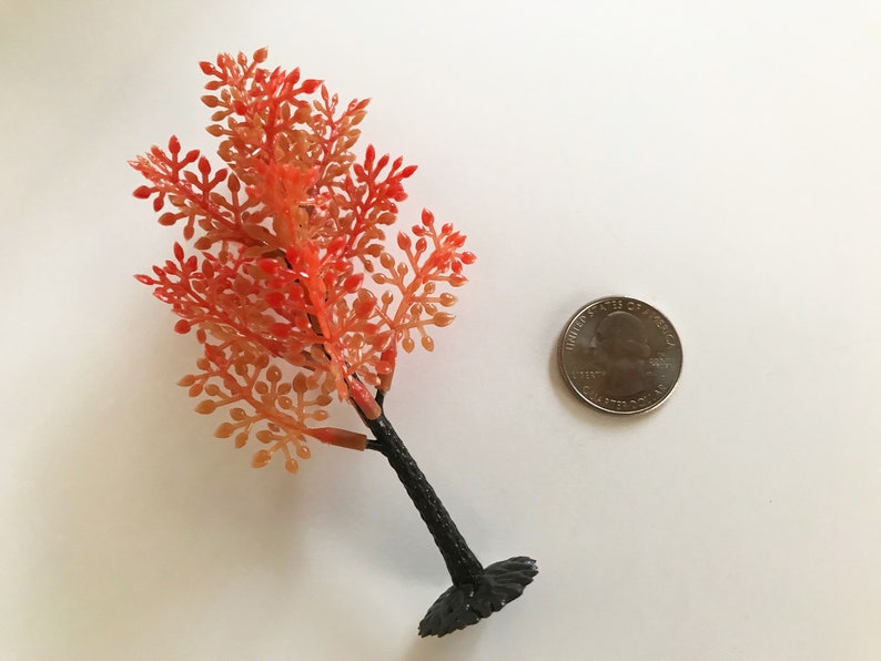May include: A small, artificial autumn tree with orange and red leaves. The tree is about the size of a 25 pence coin.