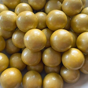 May include: A pile of golden-yellow, spherical objects with a shiny, pearl-like finish. The spheres are clustered together, filling the frame. The overall impression is of a collection of decorative or edible items.