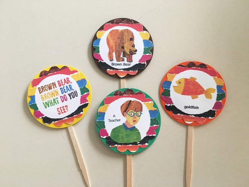 May include: Four colorful round cupcake toppers with scalloped edges. Each topper features an illustration from the children's book "Brown Bear, Brown Bear, What Do You See?" The toppers include a brown bear, a goldfish, a teacher, and the text "Brown Bear, Brown Bear. What Do You See?"