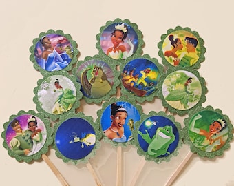 May include: A set of 10 green and blue cupcake toppers featuring characters from the Disney movie The Princess and the Frog. The toppers feature Tiana, Naveen, Ray, and Louis.